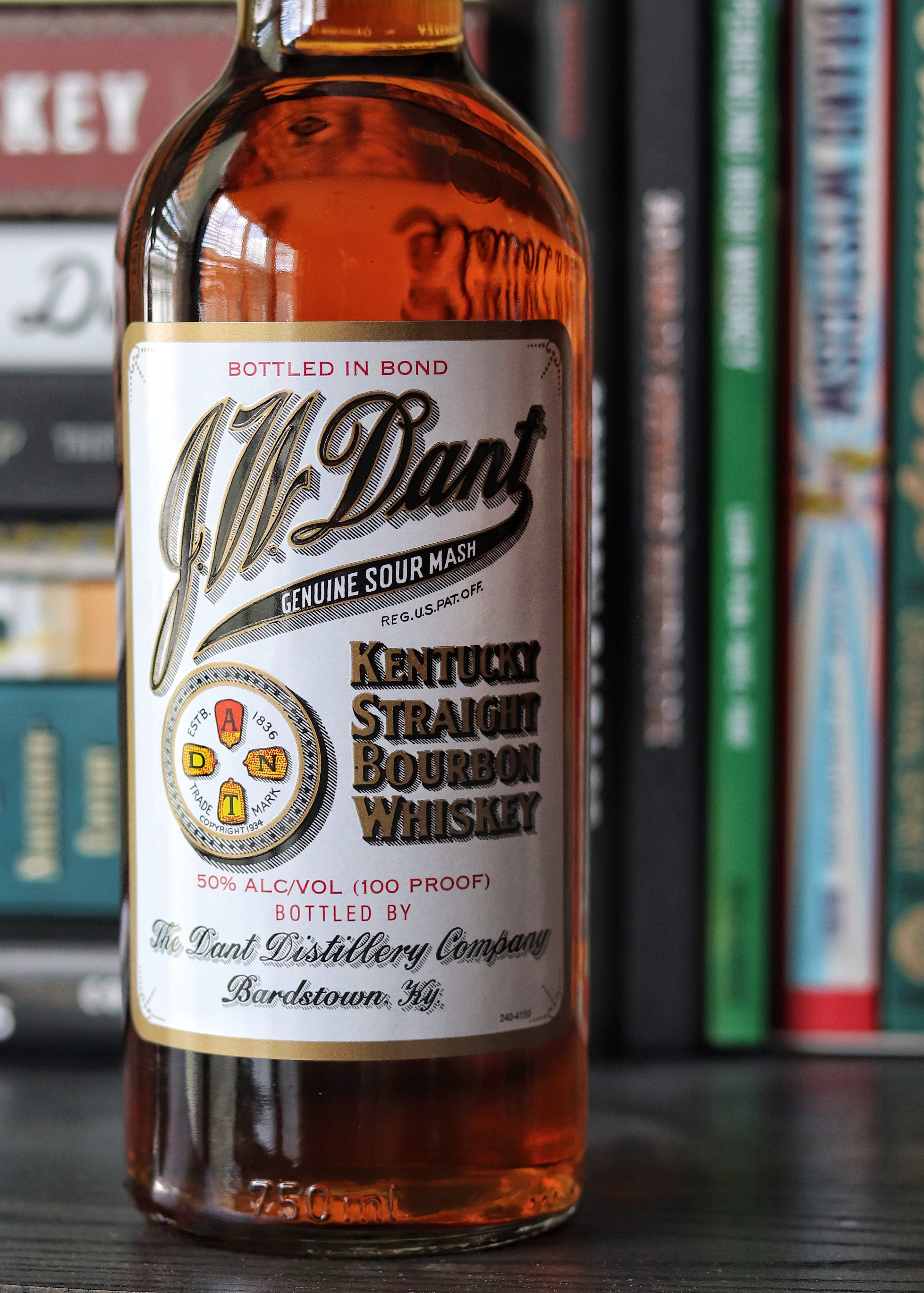A bottle of J.W. Dant Kentucky Straight Bourbon Whiskey in a library with books.