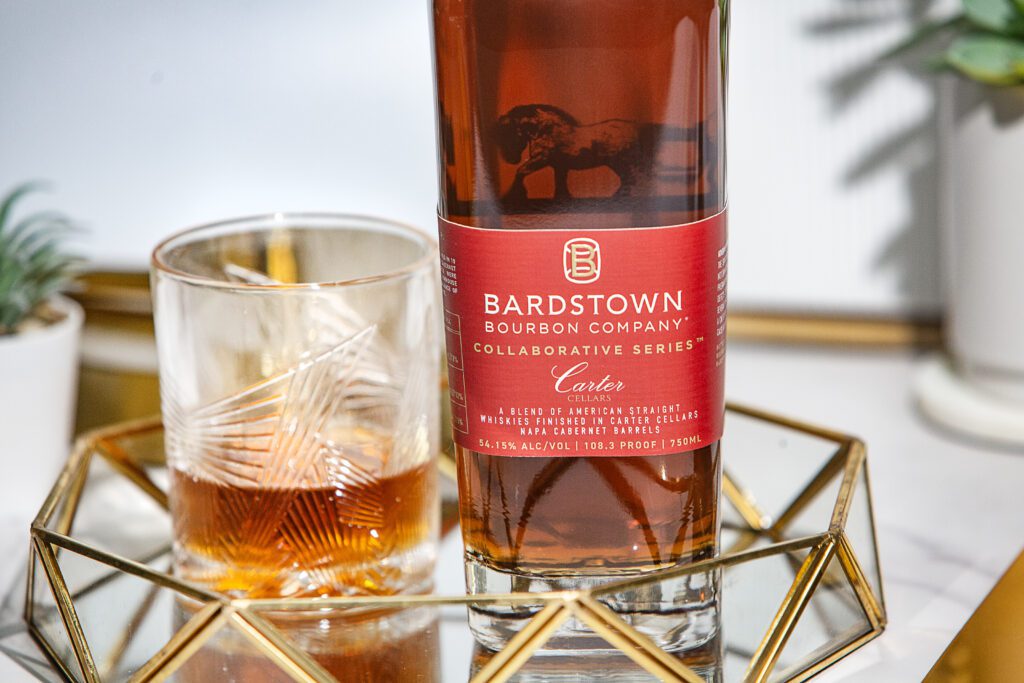 A bottle of bourbon with a low ball glass on a glass table with decor.