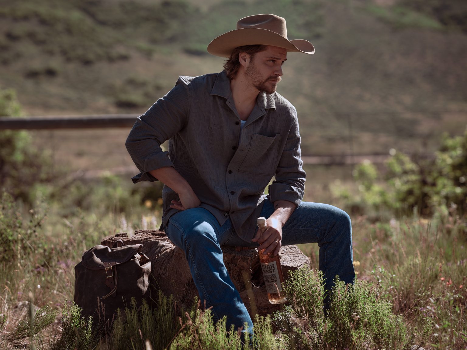 Luke Grimes on a stump with a bottle of High West